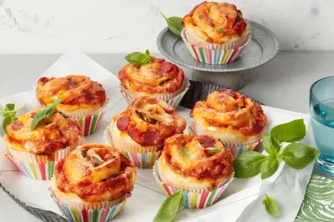 Leckere Pizza Muffins mit Salami und Käse, garniert mit frischem Basilikum.