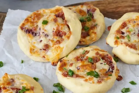 Flammkuchen Schnecken mit Speck, Käse und Frühlingszwiebeln, gebacken auf Backpapier.