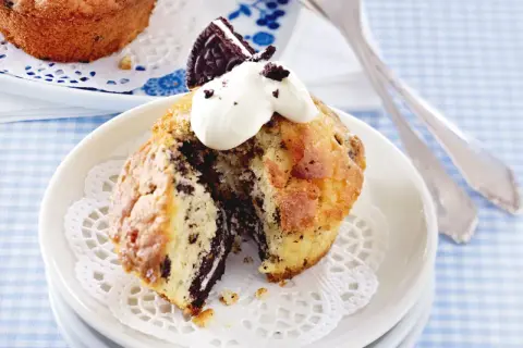 Ein aufgeschnittener Oreo Muffin mit Sahne und einem Oreo-Stück obendrauf, serviert auf einem Spitzendeckchen.
