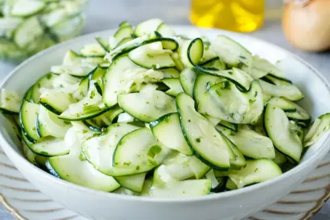 Frischer Salat aus dünn geschnittenen Zucchinischeiben, mariniert mit Kräutern und Öl. Perfekt, um Zucchini roh zu essen.