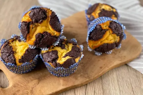 Schokoladen-Vanille-Zupfkuchen-Muffins in blauen Papierförmchen auf einem Holzbrett.