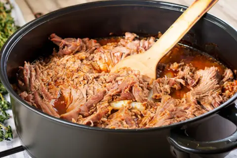 Zartes pulled pork im Dutch Oven, bereit zum Servieren. Ein Holzlöffel liegt darin.