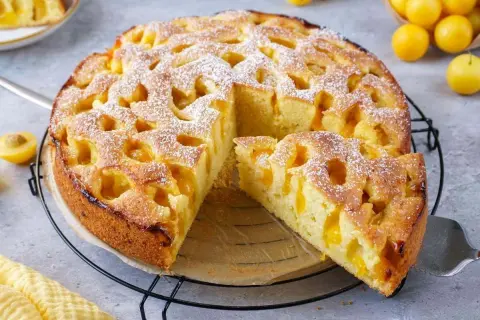 Ein goldbrauner mirabellen kuchen, mit Puderzucker bestäubt, wartet auf seine Genießer. Ein Stück ist bereits herausgeschnitten.