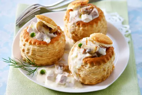 Drei Blätterteig-Schiffchen gefüllt mit cremigem Ragout Fin, garniert mit Erbsen und Dill.