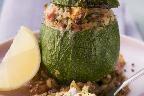 Gefüllte, runde Zucchini mit einer herzhaften Mischung aus Reis und Fleisch, serviert mit einer Zitronenspalte und Linsen.