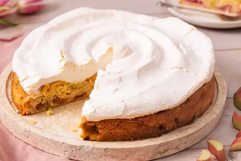 Ein köstlicher Rhabarberkuchen mit Baiser, dessen fluffige Haube leicht gebräunt ist. Ein Stück fehlt bereits.