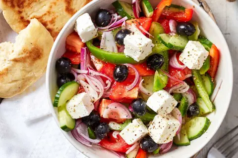 Frischer griechischer Salat mit Tomaten, Gurken, roten Zwiebeln, Oliven und Feta-Käse, serviert mit Fladenbrot.