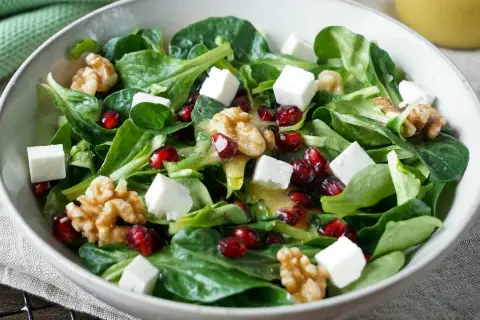 Feldsalat-Rezept: Grüner Salat mit Granatapfelkernen, Walnüssen und Feta-Würfeln, beträufelt mit einem leichten Dressing.