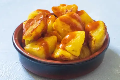 Knusprige Kartoffelstücke, überzogen mit einer würzigen Sauce, serviert als köstliche Patatas Bravas in einer kleinen Schale.
