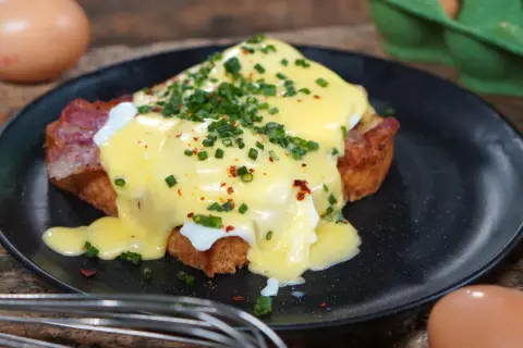 Ein köstliches Egg Benedict mit pochiertem Ei, Speck und Sauce Hollandaise, garniert mit Schnittlauch und Chiliflocken.