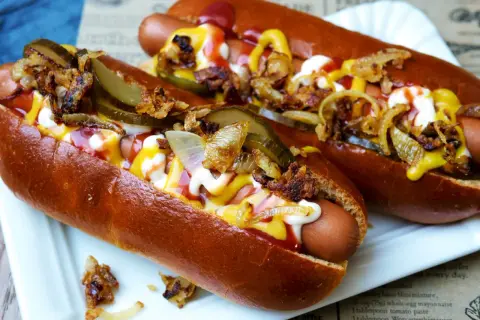 Zwei appetitliche Hot Dogs mit Senf, Ketchup, Mayonnaise, Gurken und Röstzwiebeln.