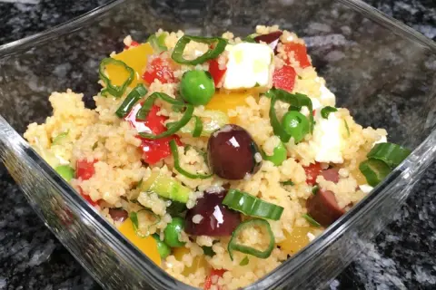 Frischer Couscous Salat mediterran mit Oliven, Paprika, Erbsen und Feta in einer Glasschüssel.