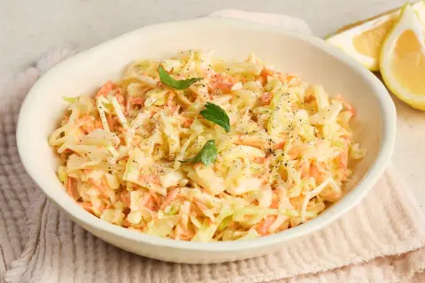 Cremiger Coleslaw Salat mit Karotten und Kohl, garniert mit Petersilie und Pfeffer. Dazu Zitronenspalten.