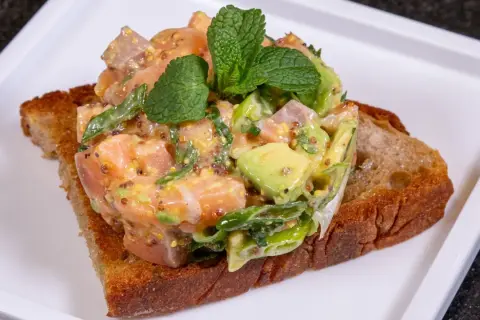Lachs-Tatar mit Avocado auf geröstetem Brot, garniert mit Minze. Ein Gericht, das selbst Sterneköche begeistert.