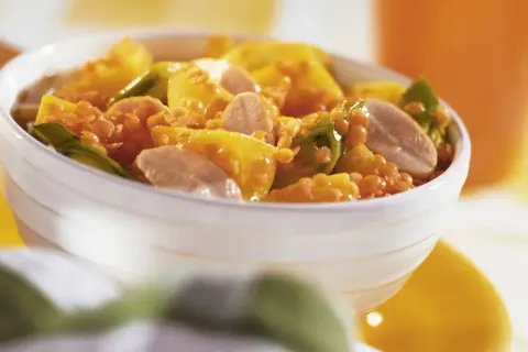 Schüssel mit einem leckeren roten Linsen Rezept, garniert mit gelben Paprikastücken und Fleischstreifen.