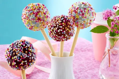 Bunte cake pops mit Schokoglasur und Streuseln in einer weißen Vase, bereit für eine fröhliche Feier.