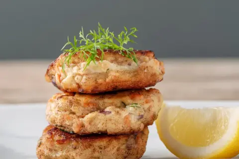 Gestapelte Fischbuletten, garniert mit Dill, neben einer Zitronenspalte. Ein leckeres Buletten Rezept.