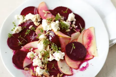 Rote Bete Salat mit Apfel, zerbröckeltem Käse und Sonnenblumenkernen auf einem weißen Teller.