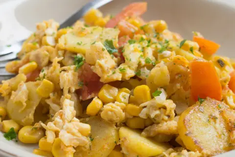 Herzhaftes Gericht mit Kartoffelscheiben, Rührei, Mais und Tomaten. Ein leckeres Beispiel für Kartoffel Gerichte.