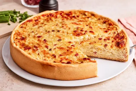 Ein goldbrauner Zwiebelkuchen mit Speck, ein Stück herausgeschnitten. Perfekt für ein Zwiebelkuchen Rezept.