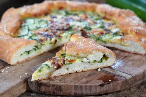 Eine köstliche Zucchini-Pizza mit goldbraunem Teig und saftiger Füllung, auf einem rustikalen Holzbrett serviert.