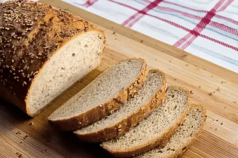 Ein frisch gebackenes Brot, perfekt für ein keto brot rezept, liegt auf einem Holzbrett. Mehrere Scheiben sind bereits abgeschnitten.