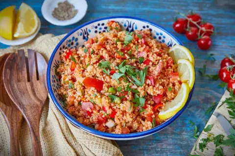 Frischer Bulgur Salat mit Tomaten, Paprika und Kräutern, garniert mit Zitronenspalten. Ein leichter Genuss!