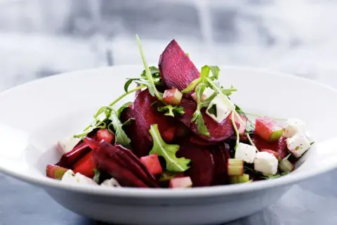 Ein köstlicher rote beete salat mit Rucola, Feta und Apfelstücken in einer weißen Schüssel.
