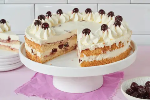 Saftiger Kuchen mit Sahne und Kirschen, perfekt zum Amarenakirschen selber machen. Ein Stück fehlt, daneben eine Schale mit Kirschen.
