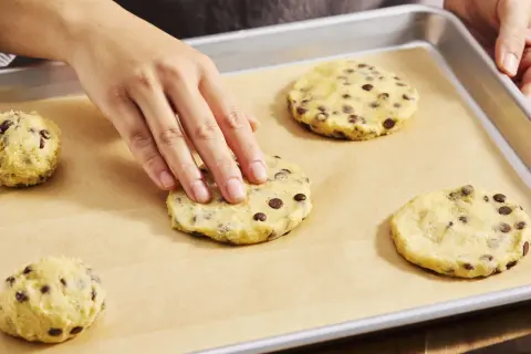 Hände formen Teig für Chocolate Chip Cookies auf einem Backblech. Der Teig ist voller Schokoladenstückchen, bereit für den cookie crumble.