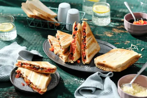 Leckere Sandwichmaker Rezepte: Getoastete Sandwiches mit Tomaten und Oliven, serviert mit Zitrone-Wasser.