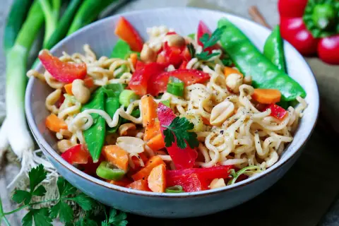 Bunter mie nudel salat mit Erdnüssen, Paprika, Zuckerschoten und Karotten, garniert mit Petersilie.