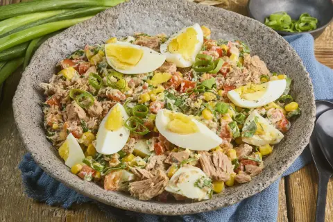 Herzhafter Thunfischsalat mit Mais, Tomaten, Ei und Frühlingszwiebeln, garniert mit hartgekochten Eierspalten.
