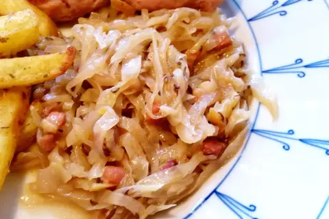 Herzhaftes bayrisch Kraut mit Speckwürfeln, serviert mit knusprigen Kartoffelspalten und einer Wurst. Ein Klassiker!