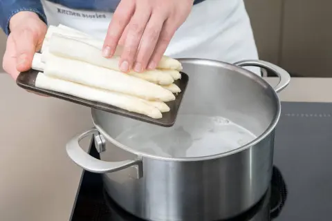 Frischer weißer Spargel wird in kochendes Wasser gegeben. So beginnt das Spargel kochen mit oder ohne Deckel.