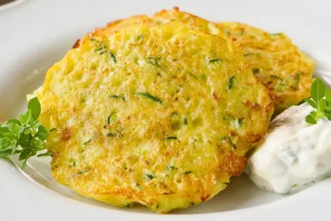 Goldbraune Zucchini-Puffer mit Kräuterquark und frischem Grün.