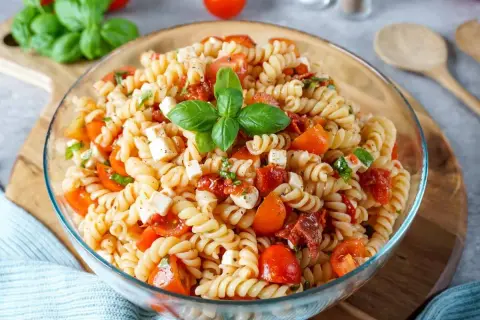 Ein köstlicher mediterraner Nudelsalat mit Fusilli, Kirschtomaten, Mozzarella und frischem Basilikum, garniert mit einem Basilikumblatt.