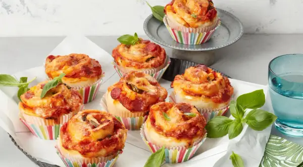 Leckere Pizza Muffins mit Salami und Käse, garniert mit frischem Basilikum.
