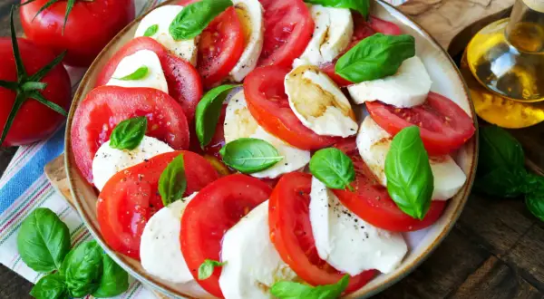 Frischer Tomate Mozzarella Salat mit Basilikum, beträufelt mit Olivenöl.