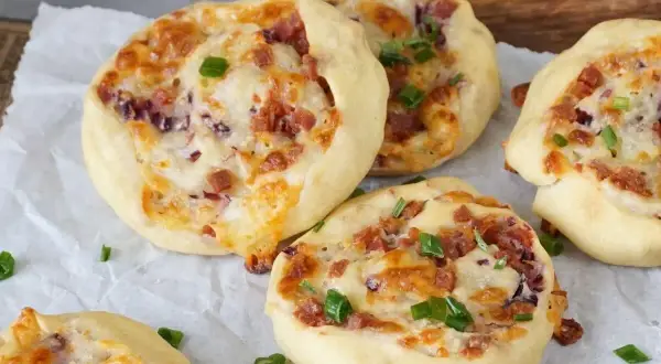 Flammkuchen Schnecken mit Speck, Käse und Frühlingszwiebeln, gebacken auf Backpapier.