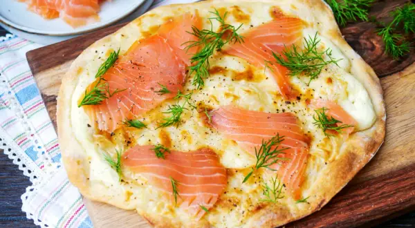 Flammkuchen mit Lachs, belegt mit zarten Lachsscheiben, geschmolzenem Käse und frischem Dill, garniert mit Pfeffer.