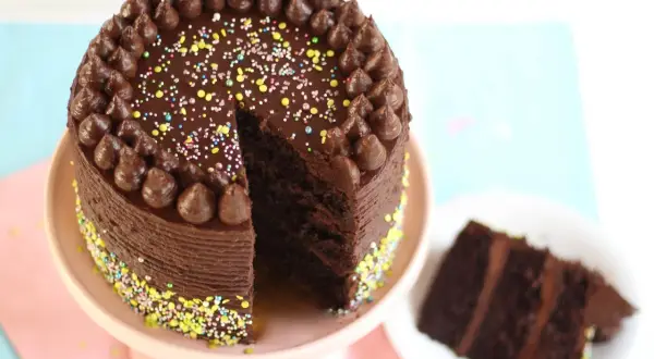 Eine köstliche Schokocreme Torte mit bunten Streuseln und Schokostückchen. Ein Stück ist bereits angeschnitten.