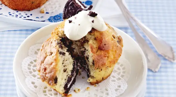 Ein aufgeschnittener Oreo Muffin mit Sahne und einem Oreo-Stück obendrauf, serviert auf einem Spitzendeckchen.