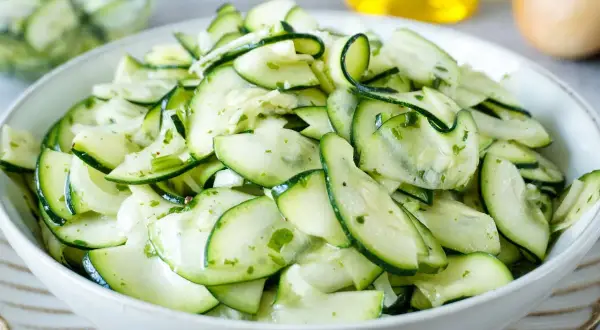 Frischer Salat aus dünn geschnittenen Zucchinischeiben, mariniert mit Kräutern und Öl. Perfekt, um Zucchini roh zu essen.