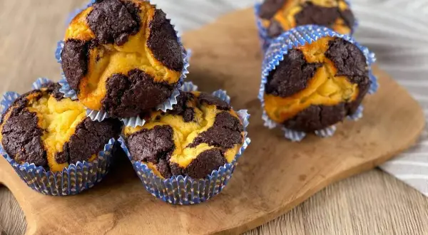 Schokoladen-Vanille-Zupfkuchen-Muffins in blauen Papierförmchen auf einem Holzbrett.