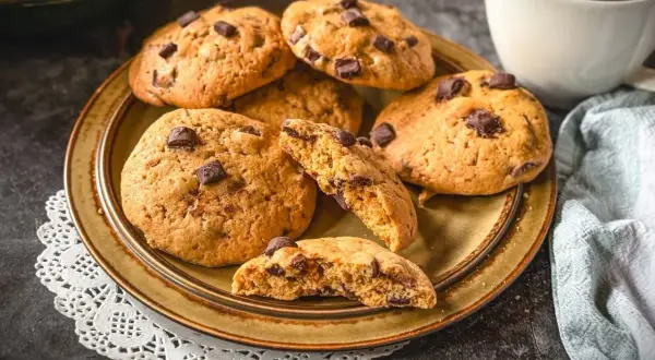 Saftige american cookies mit Schokoladenstückchen auf einem Teller, daneben eine Tasse Kaffee.