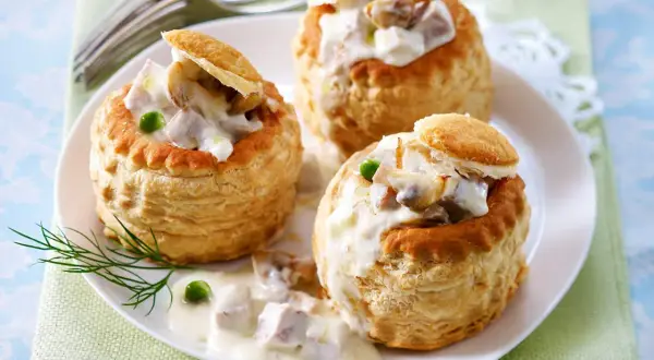 Drei Blätterteig-Schiffchen gefüllt mit cremigem Ragout Fin, garniert mit Erbsen und Dill.