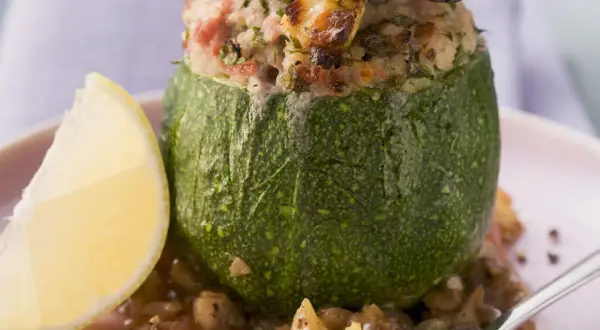 Gefüllte, runde Zucchini mit einer herzhaften Mischung aus Reis und Fleisch, serviert mit einer Zitronenspalte und Linsen.