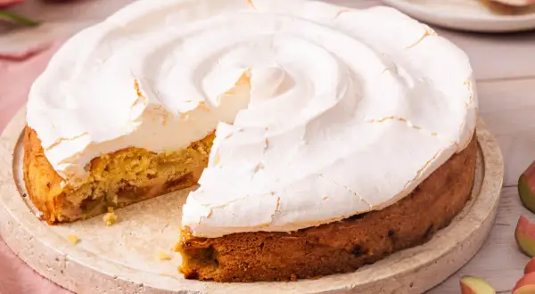 Ein köstlicher Rhabarberkuchen mit Baiser, dessen fluffige Haube leicht gebräunt ist. Ein Stück fehlt bereits.