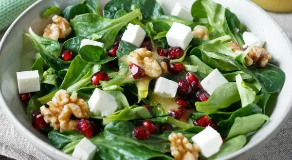 Feldsalat-Rezept: Grüner Salat mit Granatapfelkernen, Walnüssen und Feta-Würfeln, beträufelt mit einem leichten Dressing.